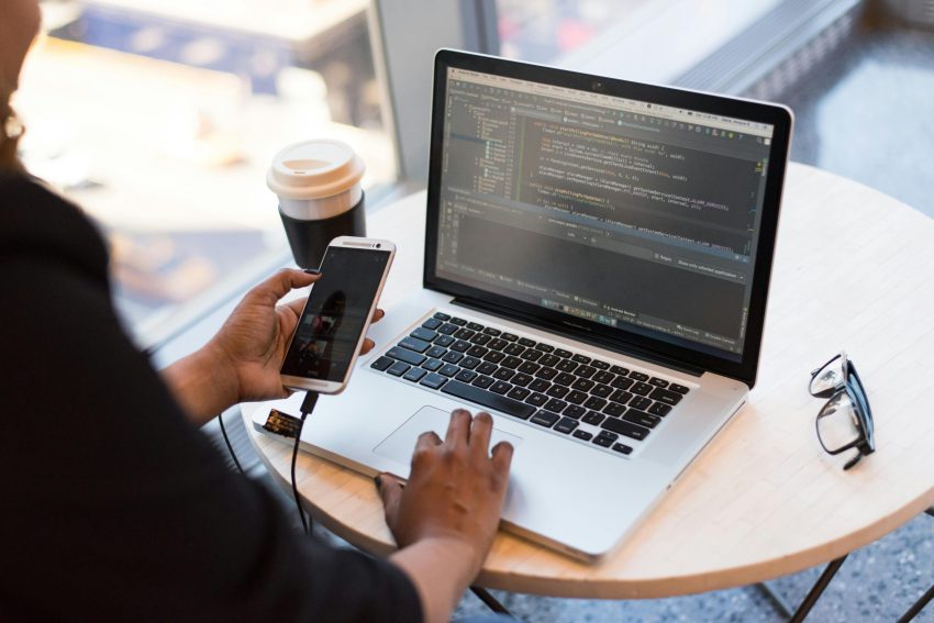 Person holding smartphone while using laptop